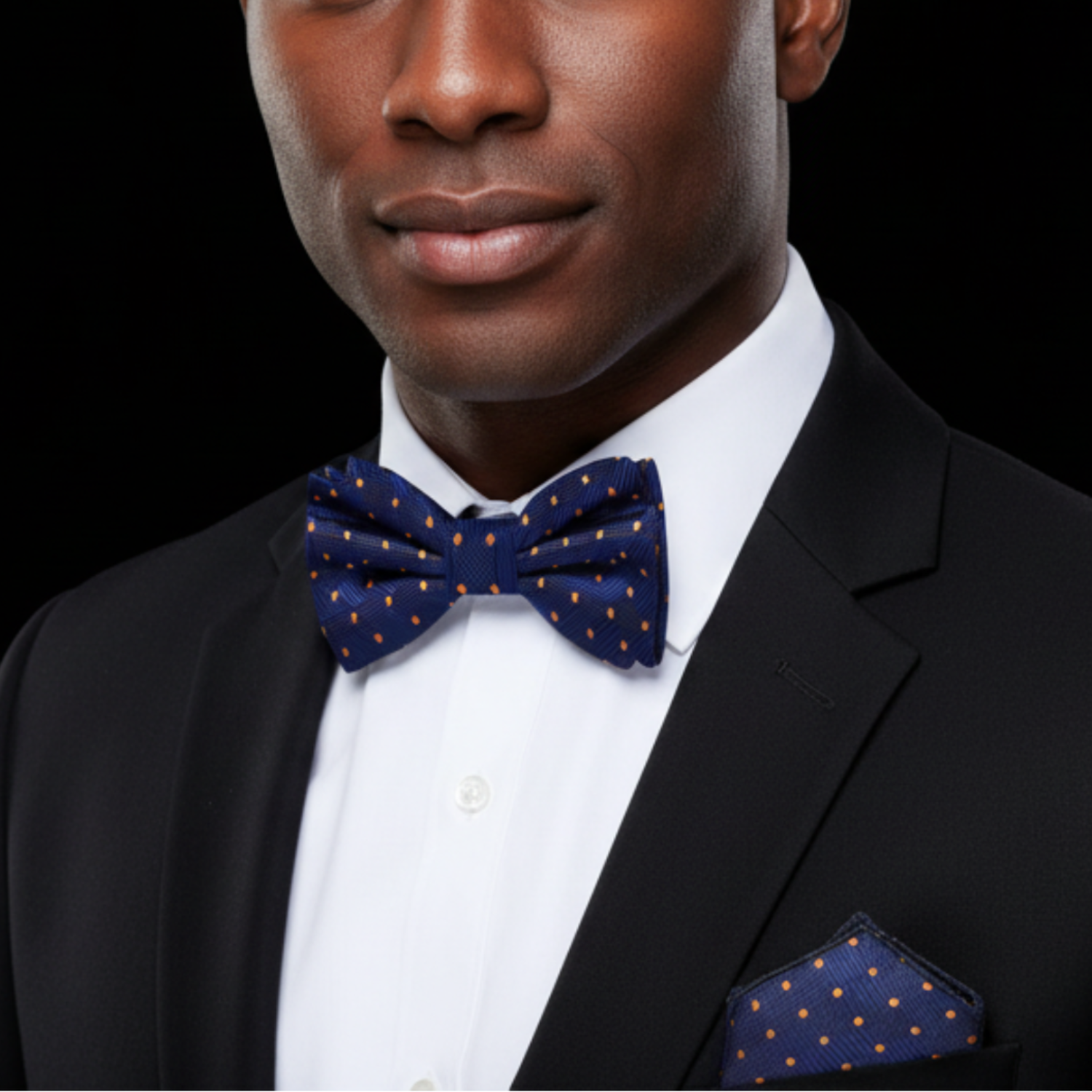 Man wearing a black suit with a blue bow tie and matching pocket square on a black background