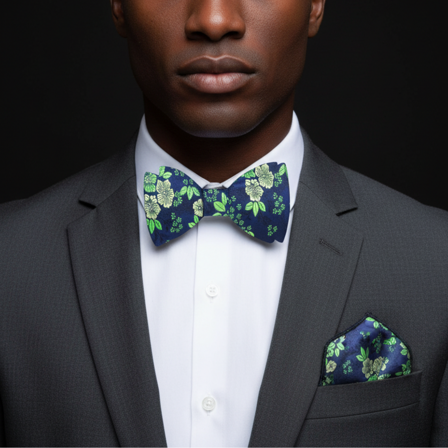 Man wearing a gray suit with a floral bow tie and pocket square on a black background