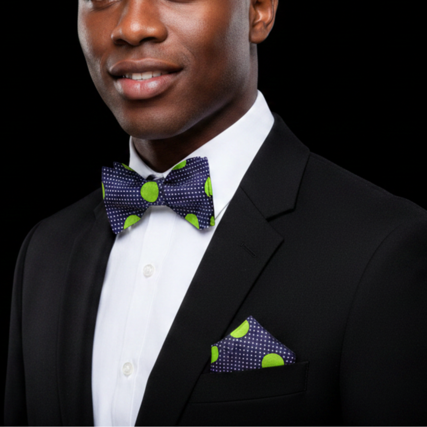 Man wearing a black suit with a purple bow tie and matching pocket square on a black background