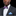 Man wearing a dark suit with a white shirt, plaid bow tie, and blue pocket square on a black background