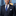 Man wearing a navy suit with a blue tie and white shirt, standing in front of a cityscape.