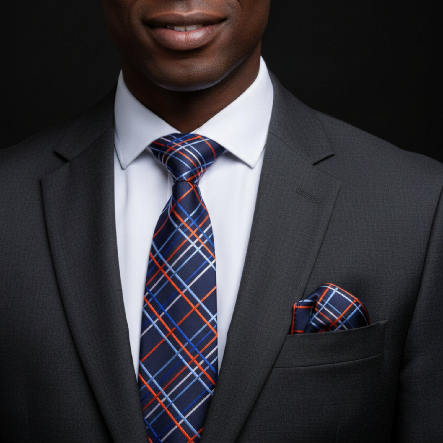 Man wearing a dark gray suit with a blue and orange plaid tie and pocket square on a black background