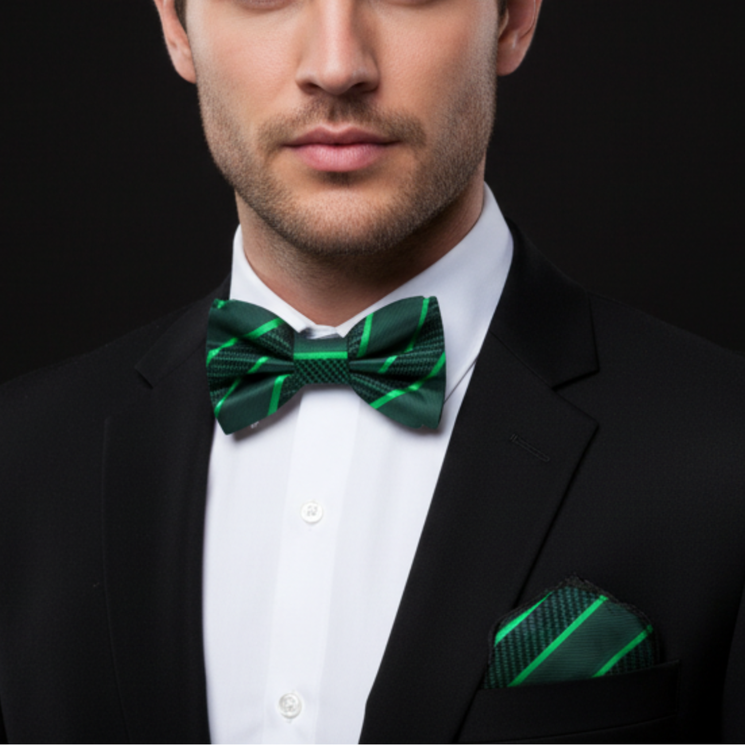 Man wearing a black suit with a green bow tie and matching pocket square on a black background