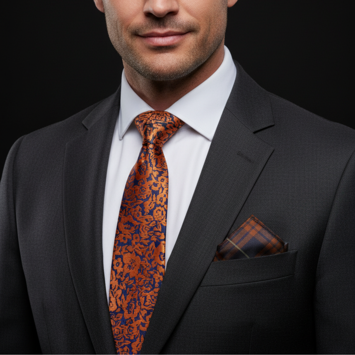 Man wearing a dark suit with an orange and blue patterned tie and pocket square on a black background