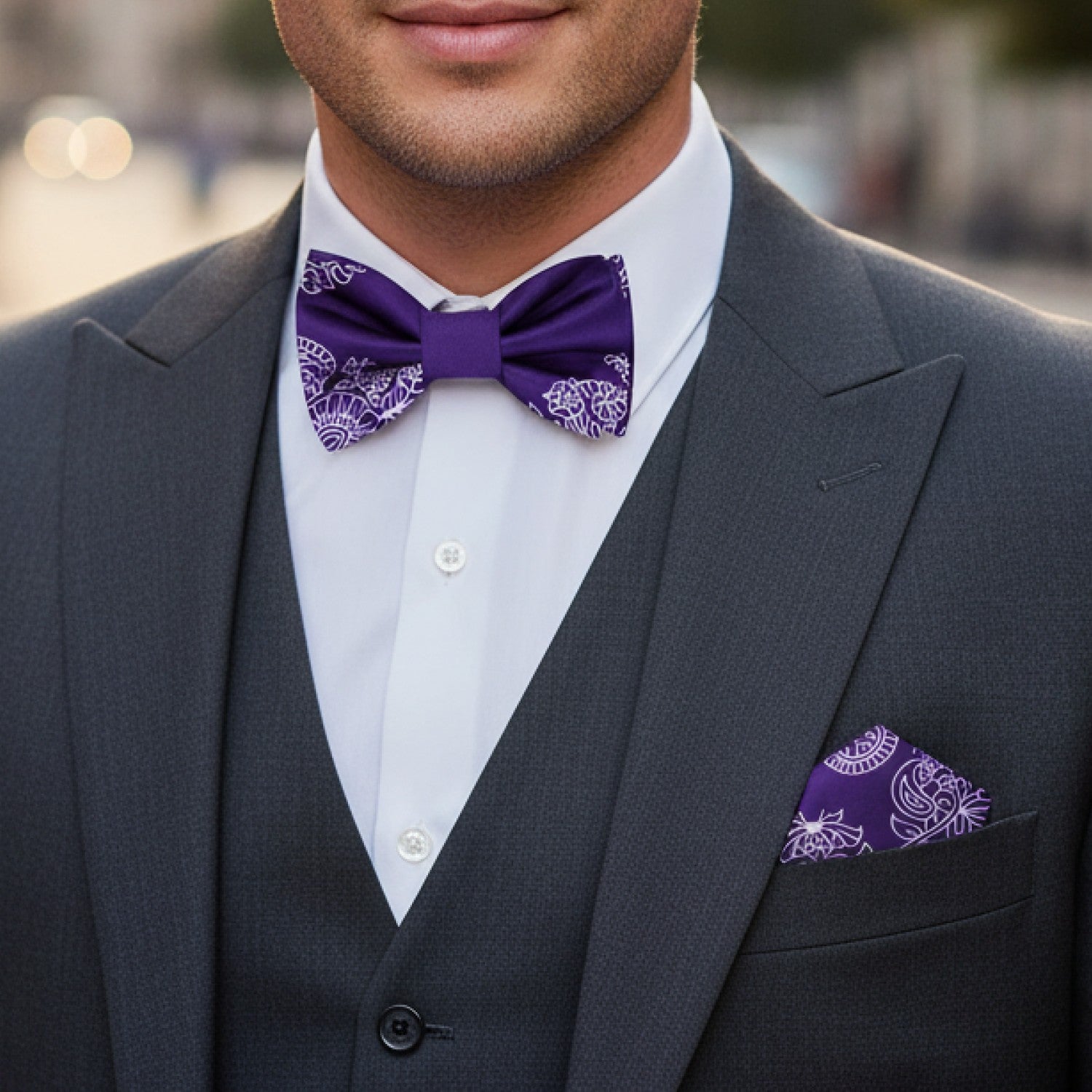 Man wearing a gray suit with a purple bow tie and matching pocket square.