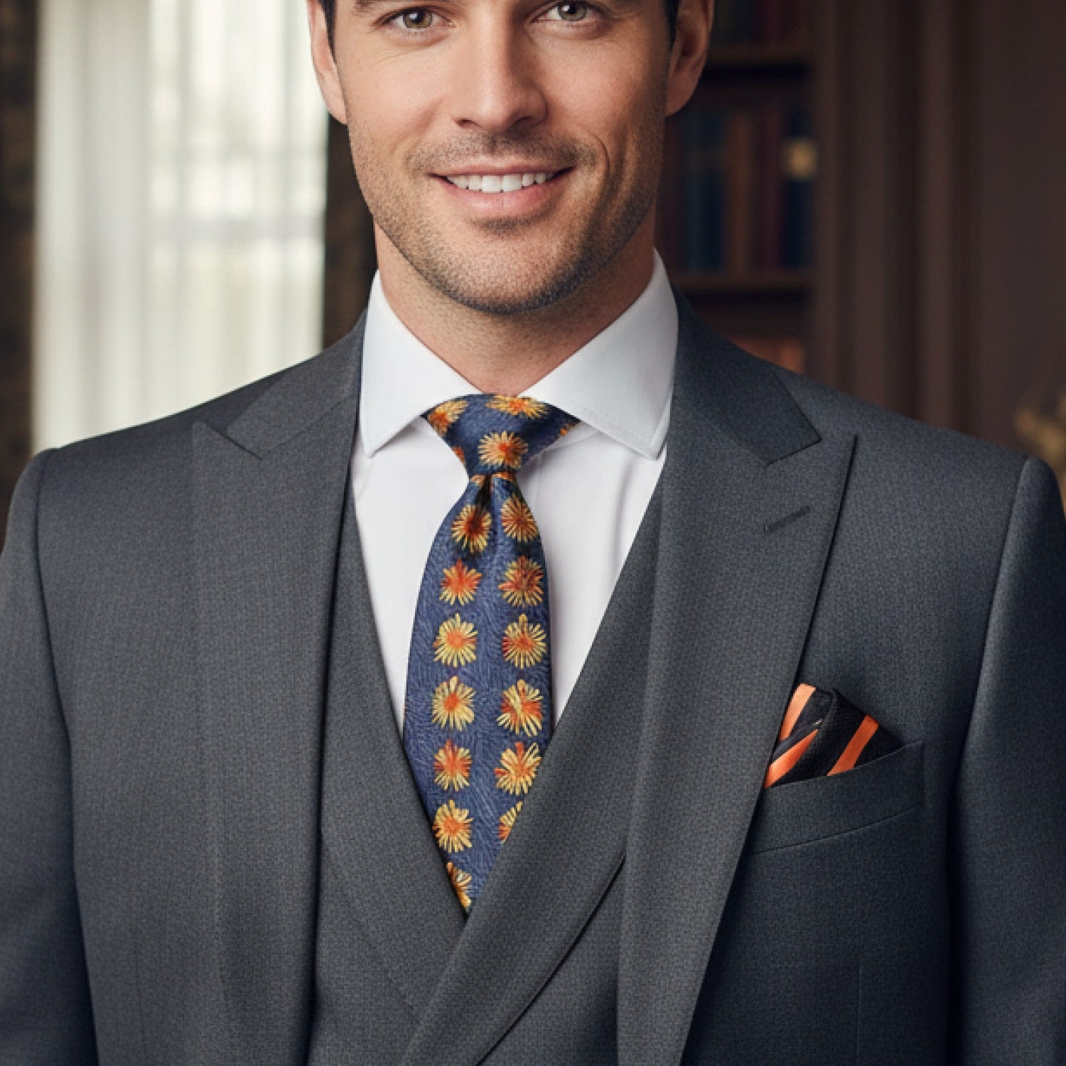 Man wearing a gray suit with a colorful tie and pocket square indoors.