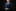Young boy in a formal navy suit with a green tie against a black background