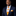 Man wearing a navy suit with an orange and white striped tie and matching pocket square on a black background