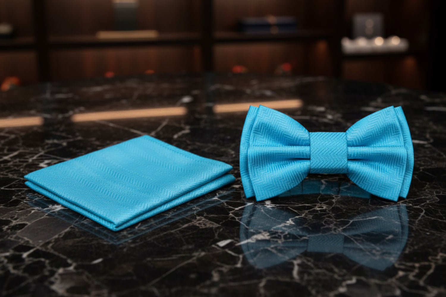 A matching light blue bow tie and pocket square set with a subtle herringbone pattern, displayed on a clean white background.