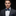 Man wearing a dark suit with a colorful bow tie and pocket square against a black background
