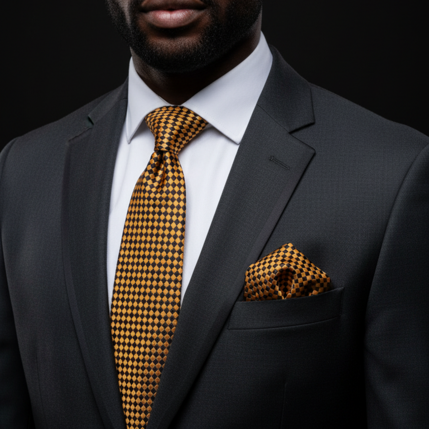 Man wearing a dark suit with a yellow patterned tie and pocket square against a black background