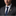 Man wearing a gray suit with a blue tie and decorative lapel pin on a black background