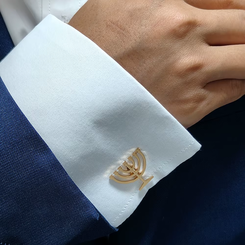 Close-up of a cufflink with a Menorah design on a white cuff against a blue fabric background.