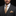 Man wearing a dark suit with a gold tie and pocket square against a black background