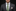 Man wearing a dark suit with a green tie and pocket square on a black background