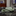 Folded green patterned handkerchief on a marble surface with ties hanging in the background
