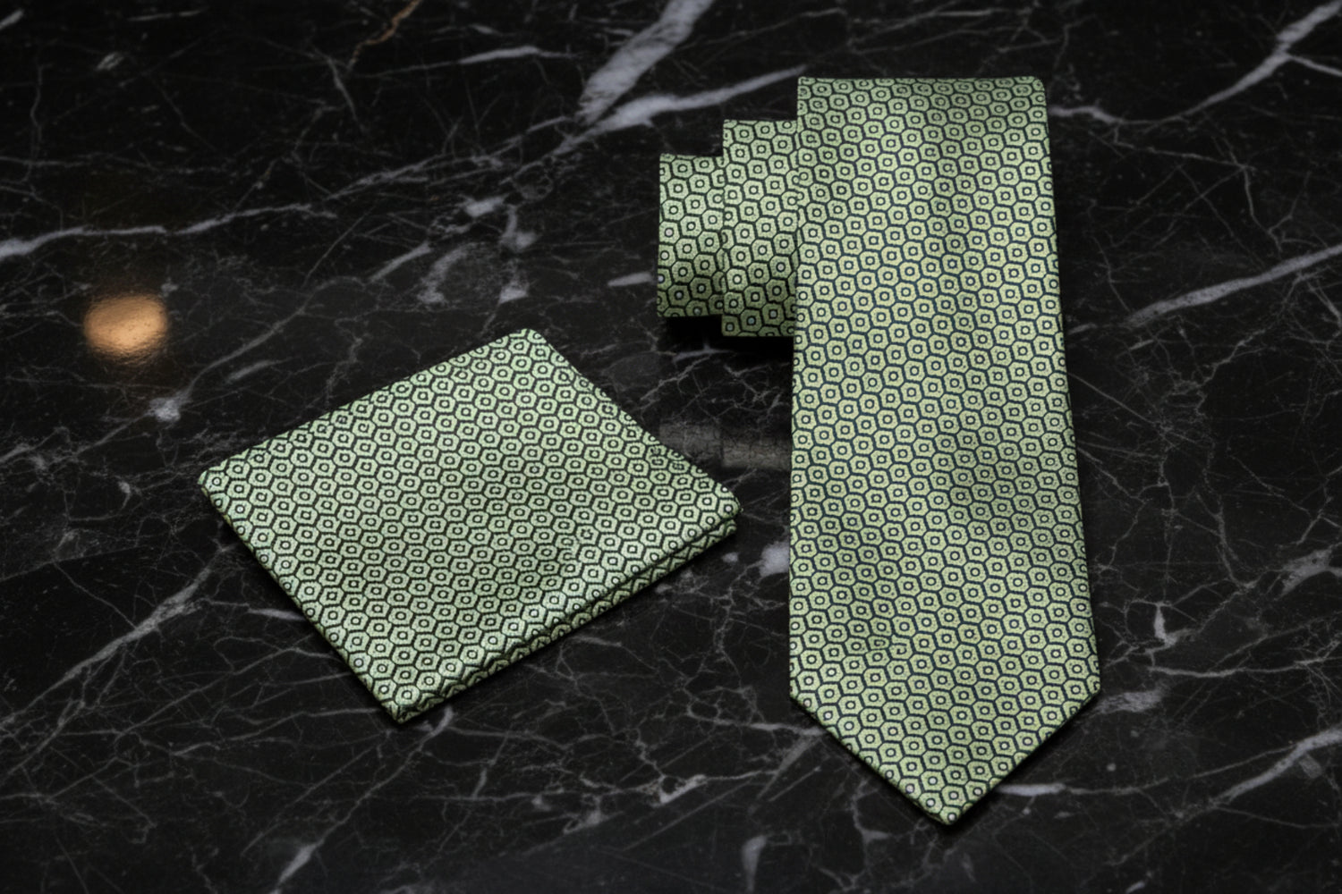 Green patterned tie and pocket square on a dark marble surface