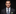 Man wearing a dark suit with a blue green floral tie and green pocket square on a black background