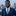 Man in a blue suit with a green tie standing in front of a city skyline.