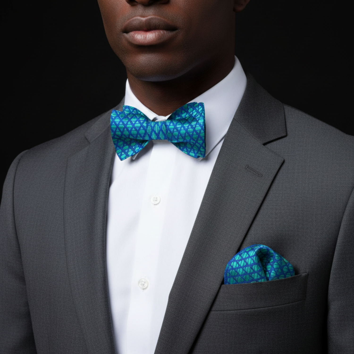 Man wearing a gray suit with a blue patterned bow tie and pocket square on a black background