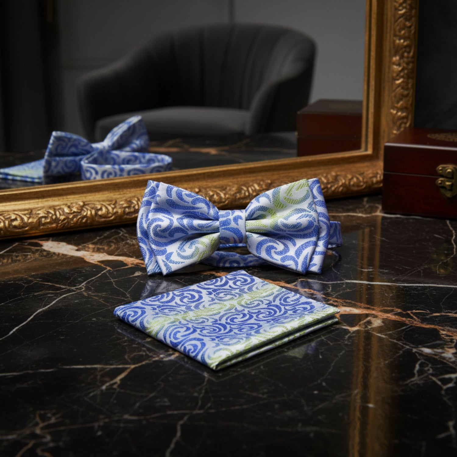 A matching men's formal accessory set featuring a self-tie bow tie and a folded pocket square, both decorated with a blue and light green paisley swirl pattern on a white base.