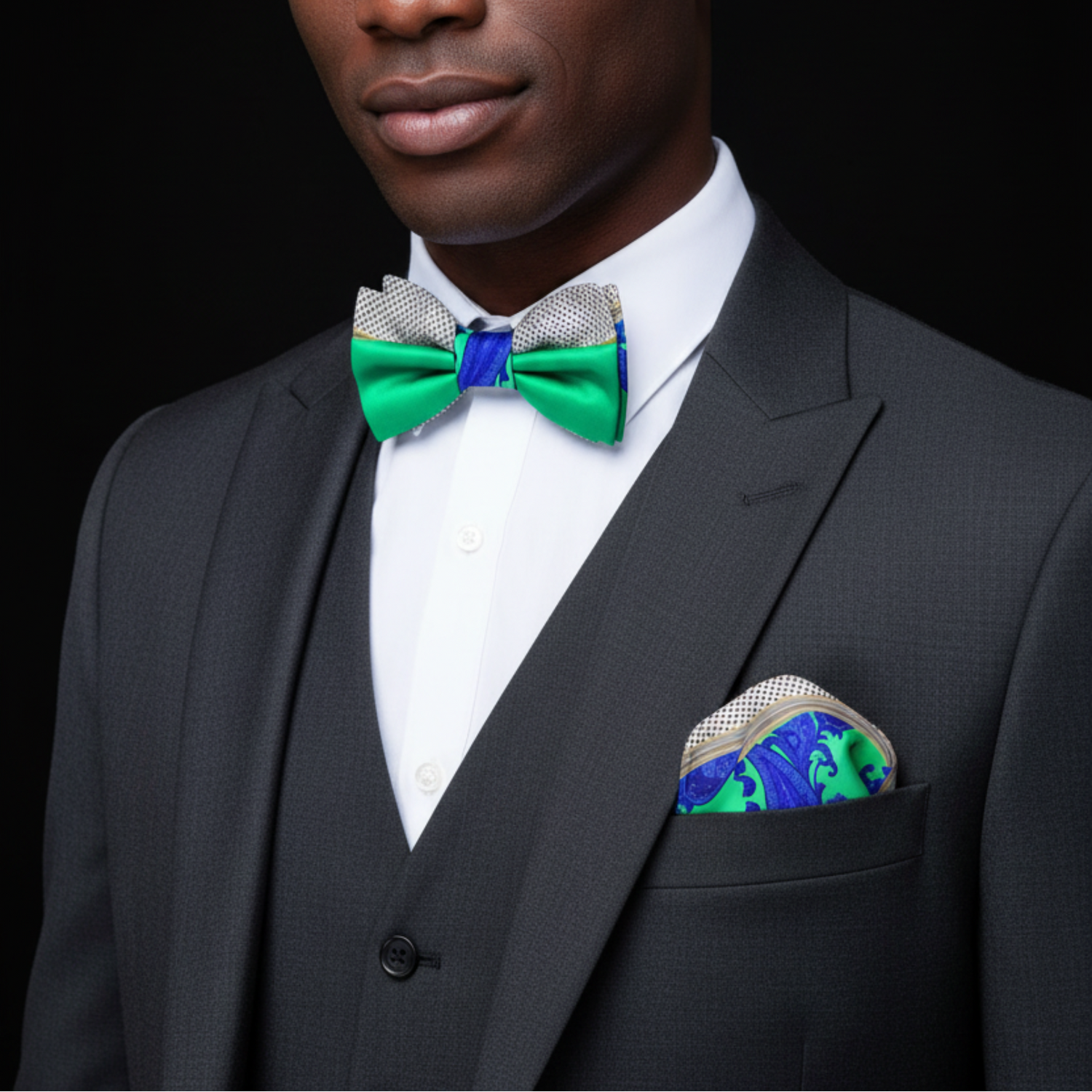 Man wearing a black suit with a green bow tie and matching pocket square against a black background