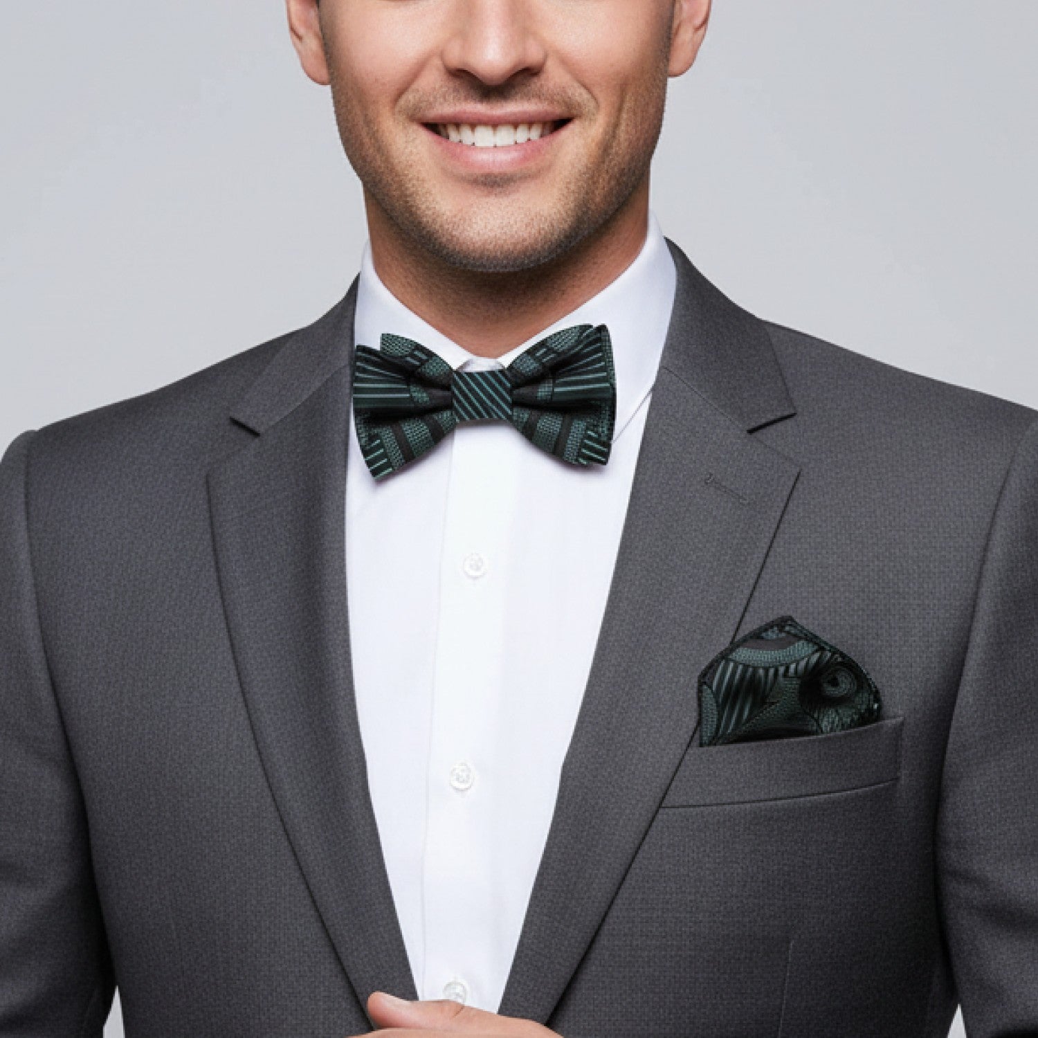 Man wearing a gray suit with a green bow tie and pocket square against a gray background
