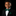 A young boy wearing a black suit jacket, white dress shirt, and a green patterned bow tie with a matching green pocket square, set against a solid black background.
