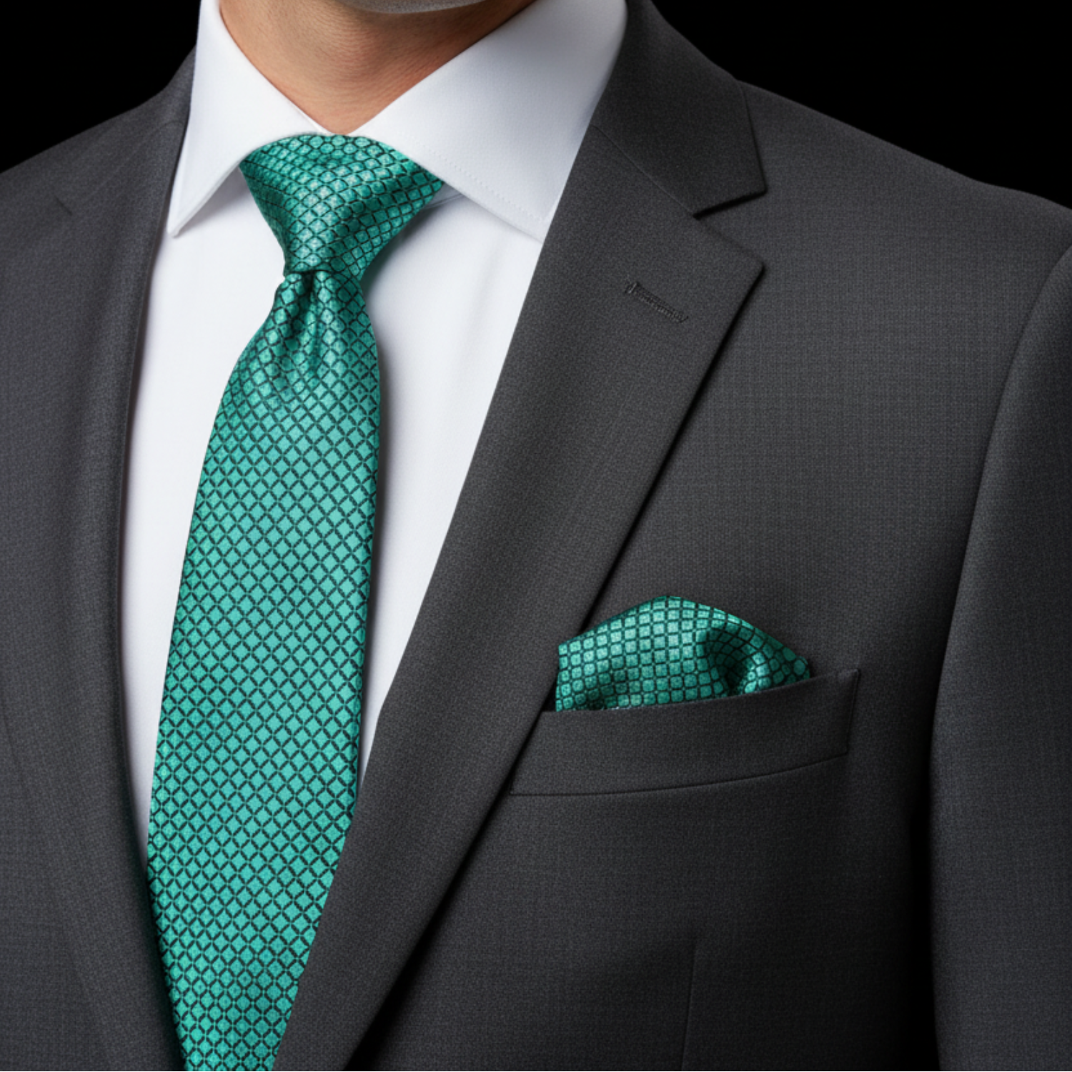 Man wearing a gray suit with a green tie and pocket square against a black background