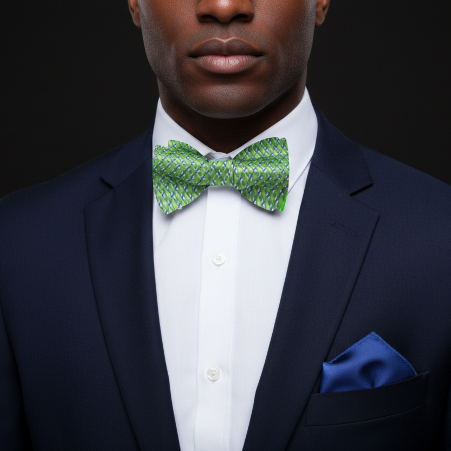 A green and blue check pattern bow tie displayed above a white shirt collar, paired with a blue pocket square.