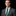 Man wearing a gray suit with a green tie and pocket square on a black background