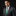 Man wearing a gray suit with a green tie and pocket square on a black background