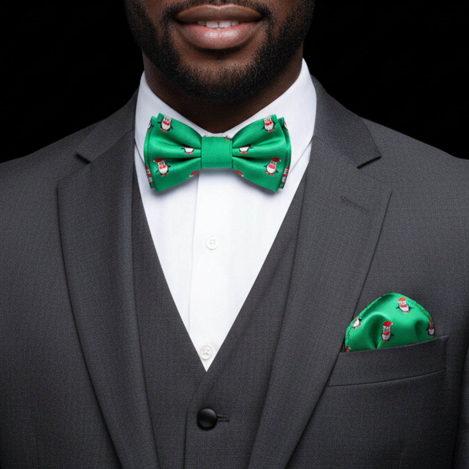 Man wearing a gray suit with a green bow tie and matching pocket square on a black background