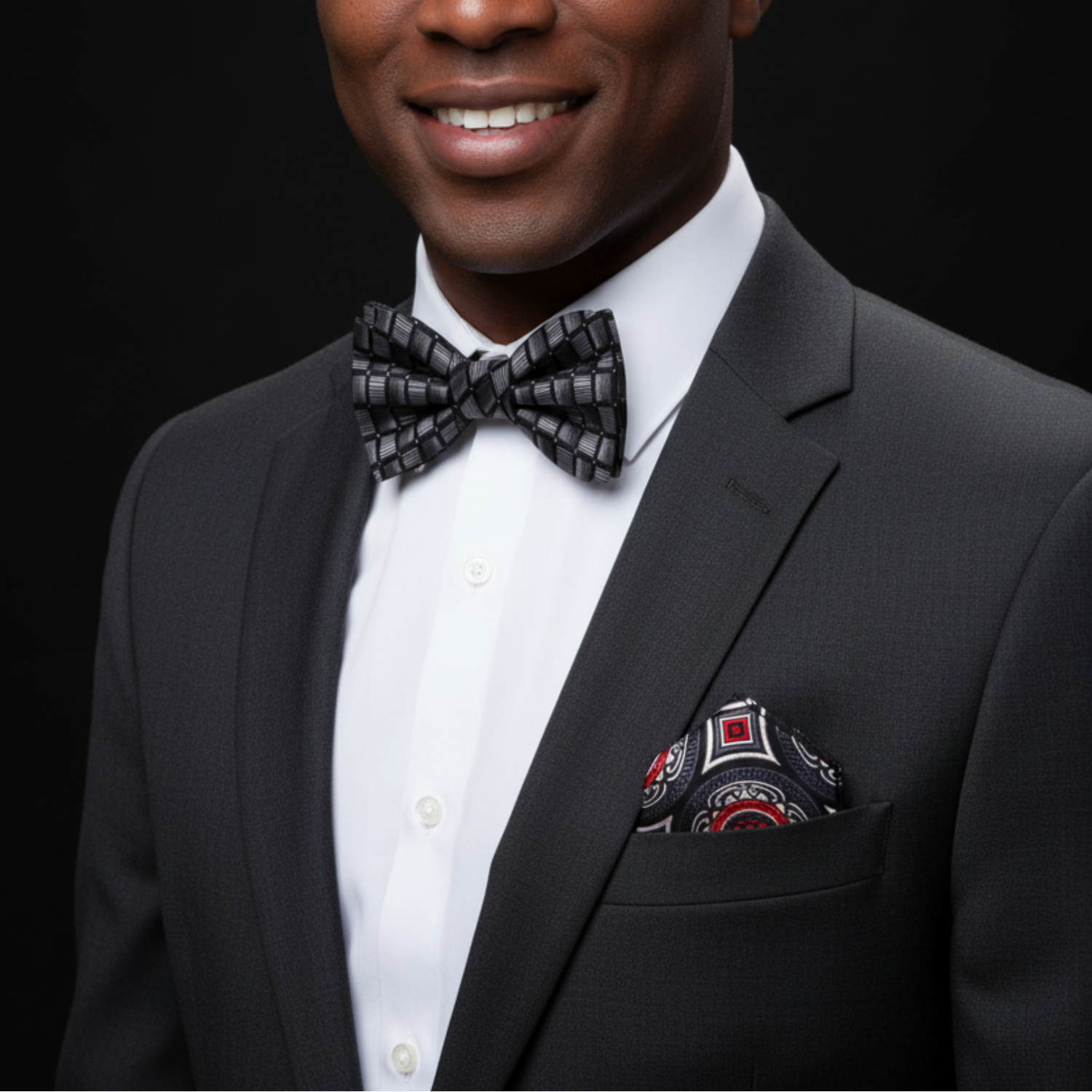 Man wearing a gray suit with a patterned bow tie and pocket square on a black background