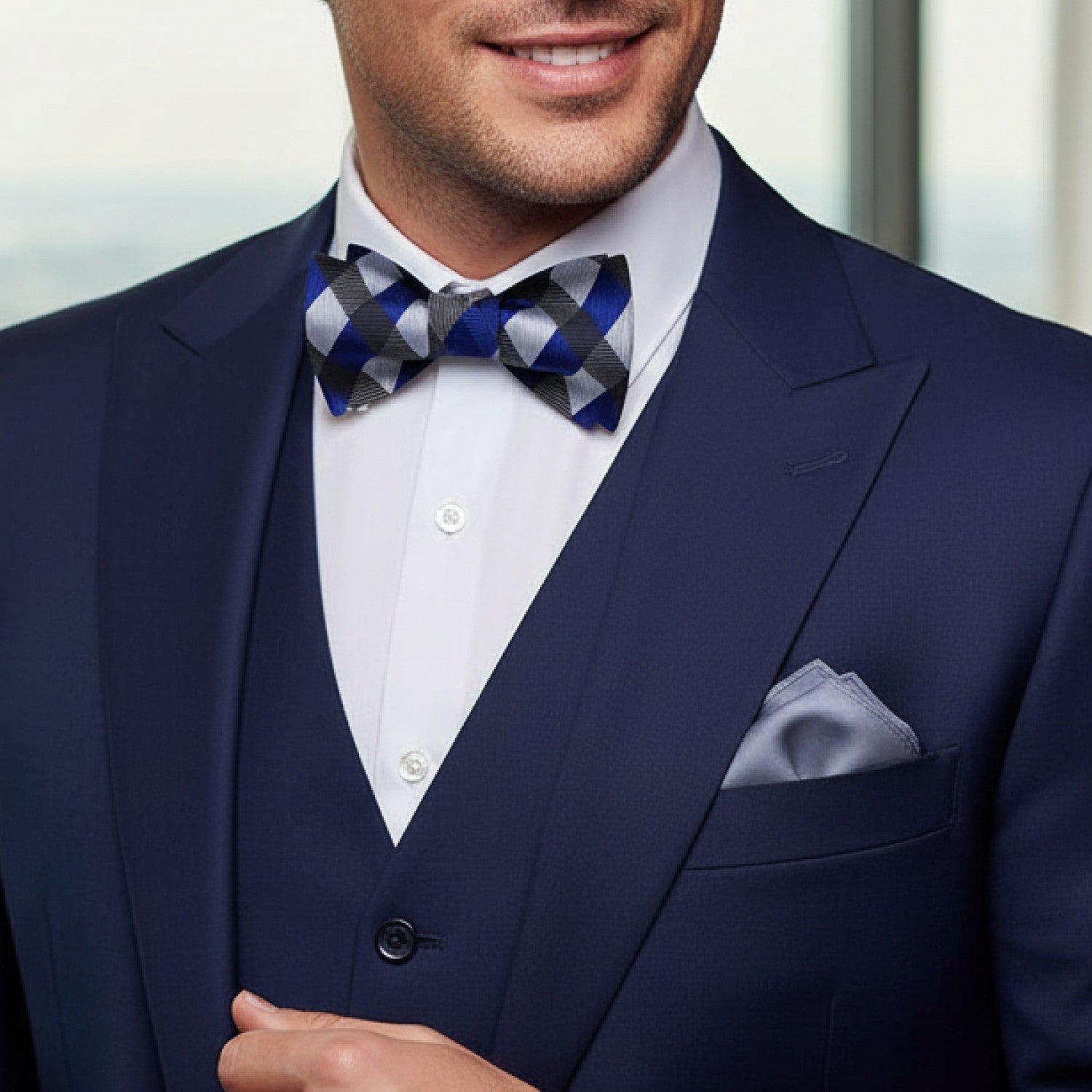 Man wearing a navy suit with a checkered bow tie and pocket square.