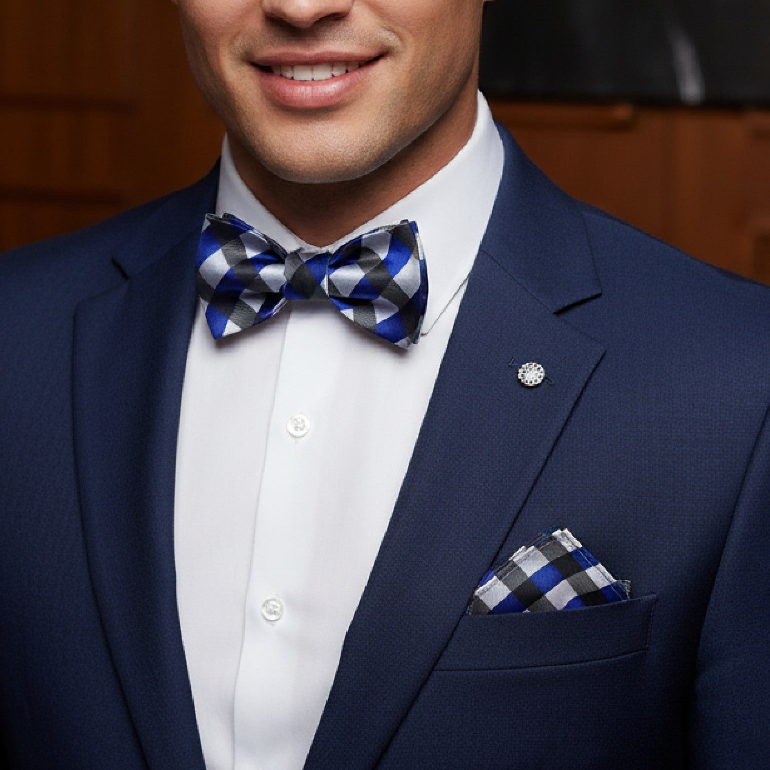 Man wearing a navy suit with a checkered bow tie and pocket square.