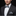 Man wearing a black suit with a plaid bow tie and pocket square on a dark background