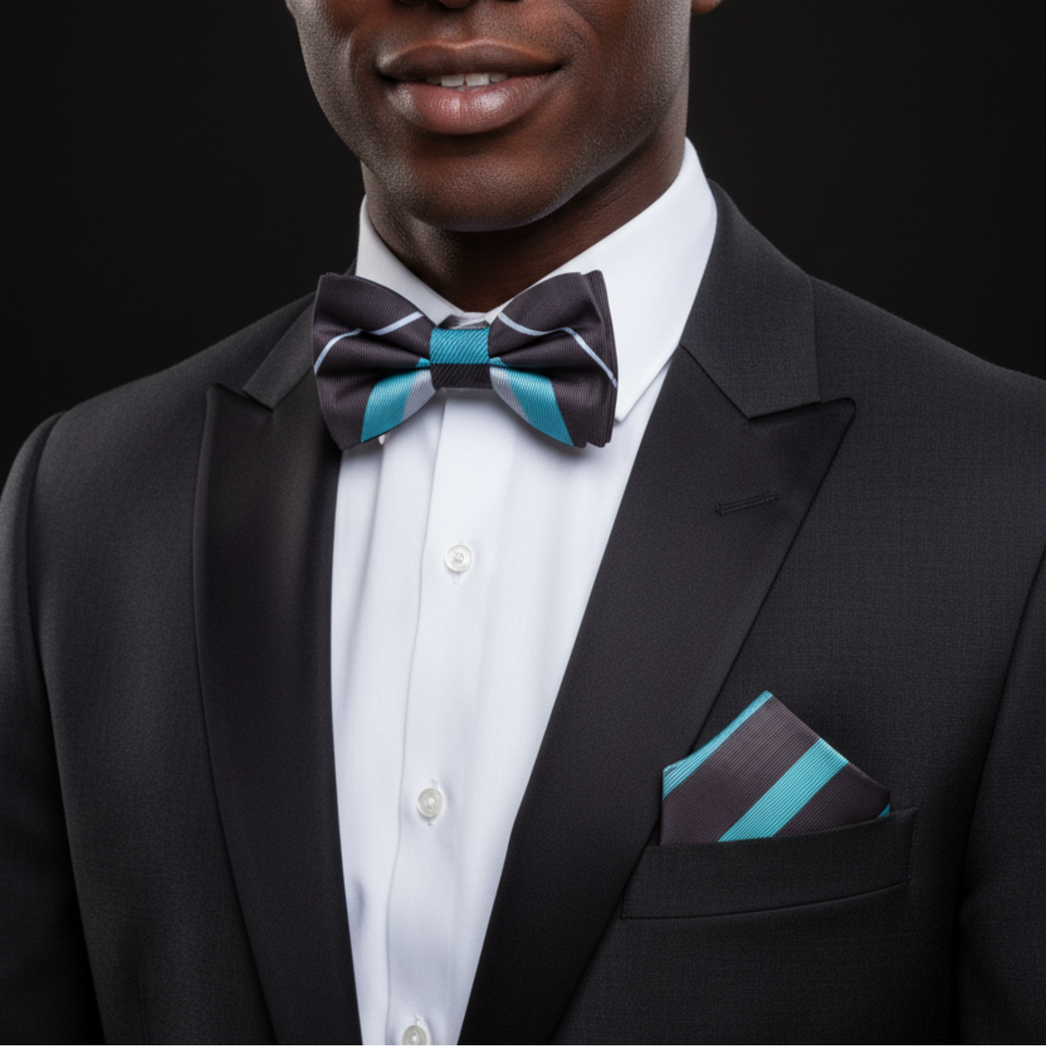 Man wearing a black suit with a white shirt, black and blue bow tie, and matching pocket square on a black background.