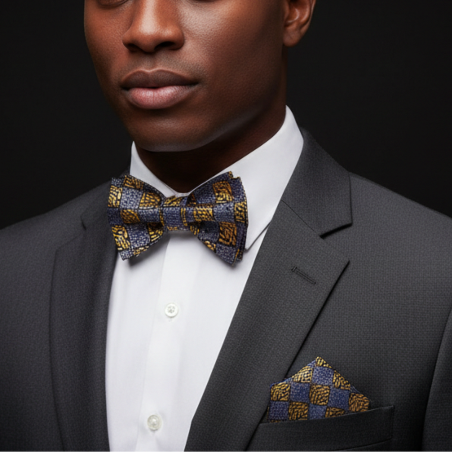 Man wearing a gray suit with a patterned bow tie and pocket square against a black background