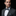 Man wearing a black suit with a patterned bow tie and pocket square on a black background