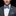 Man wearing a gray suit with a blue plaid bow tie and pocket square against a black background
