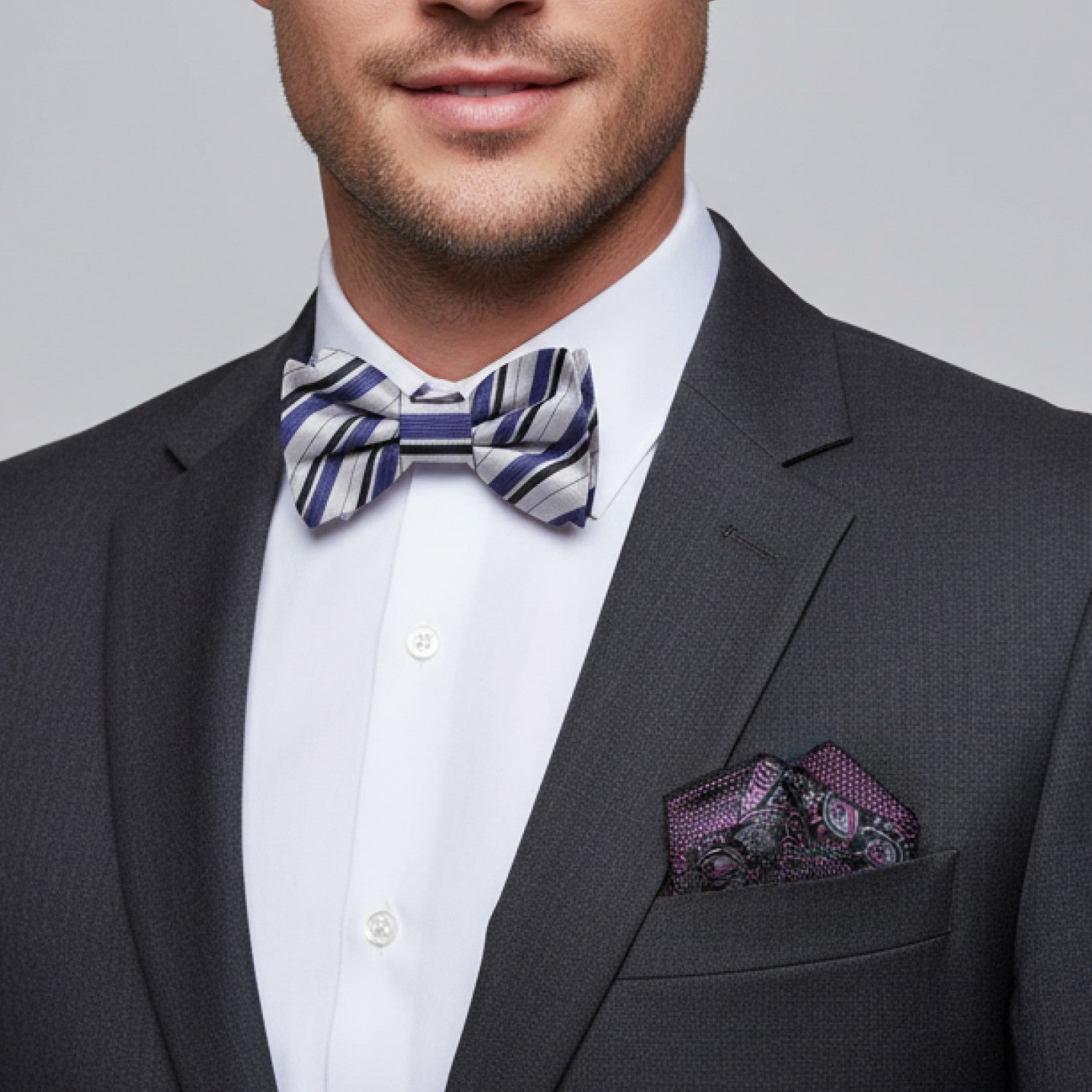 Man wearing a gray suit with a patterned bow tie and pocket square on a gray background