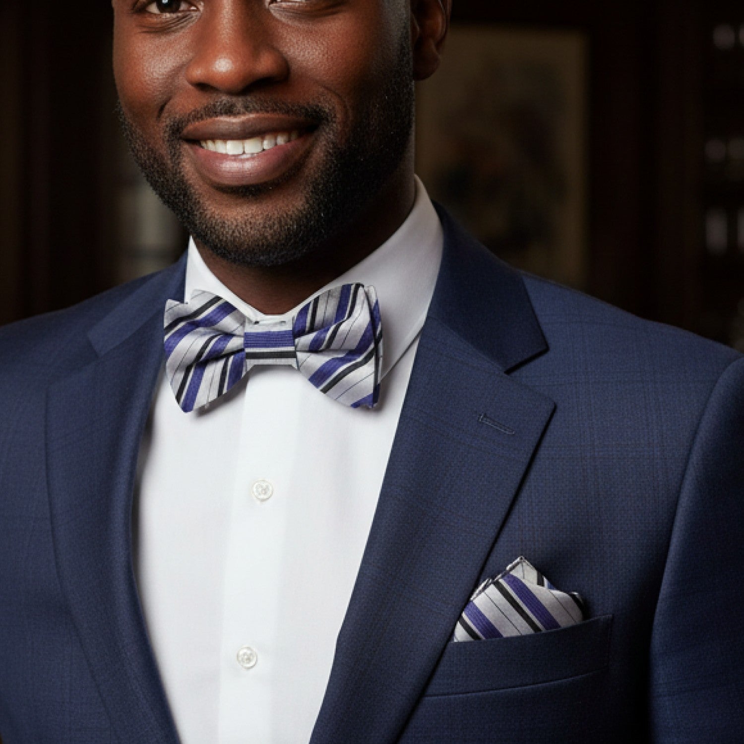 Man wearing a blue suit with a striped bow tie and pocket square.