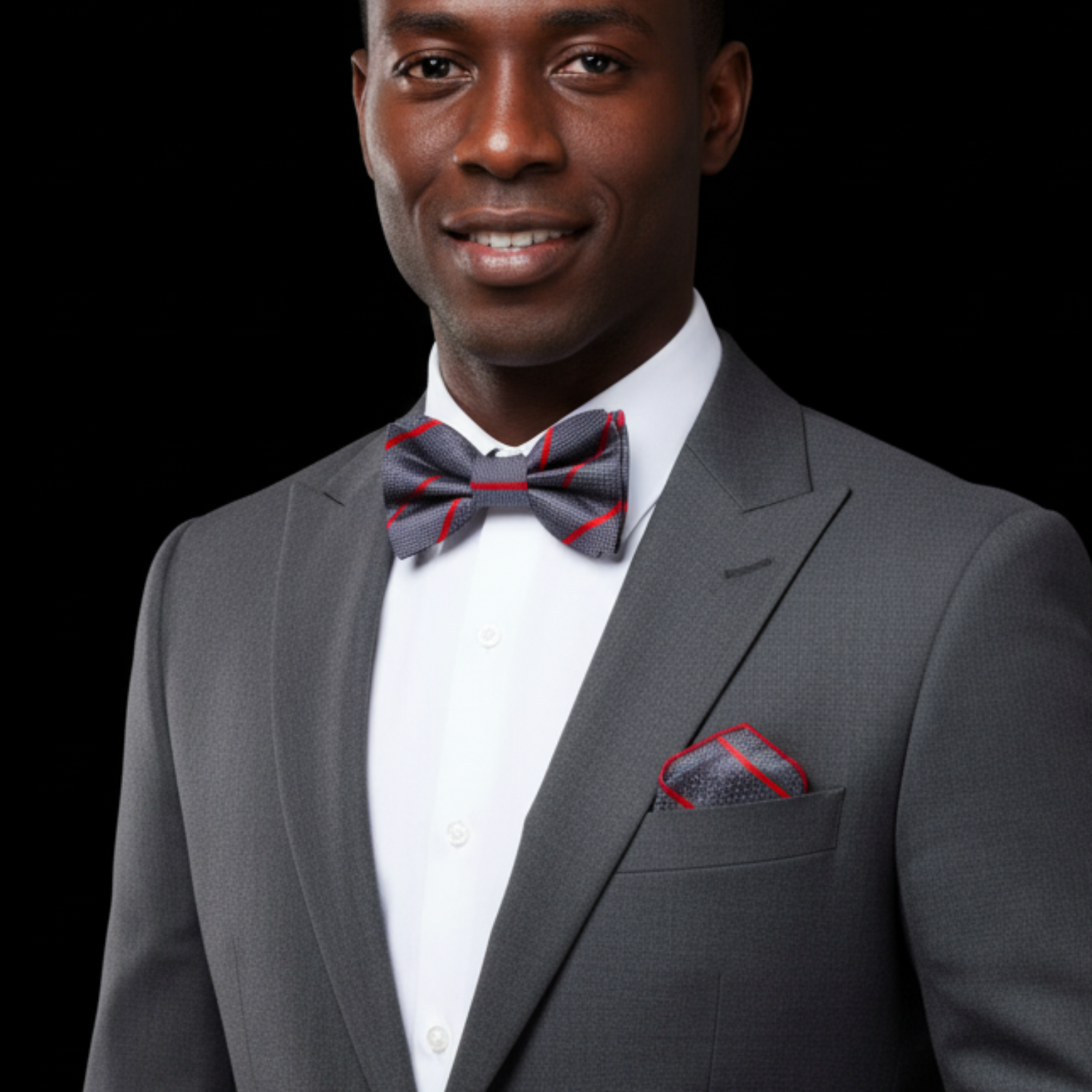 Man wearing a gray suit with a red and grey bow tie and pocket square on a black background
