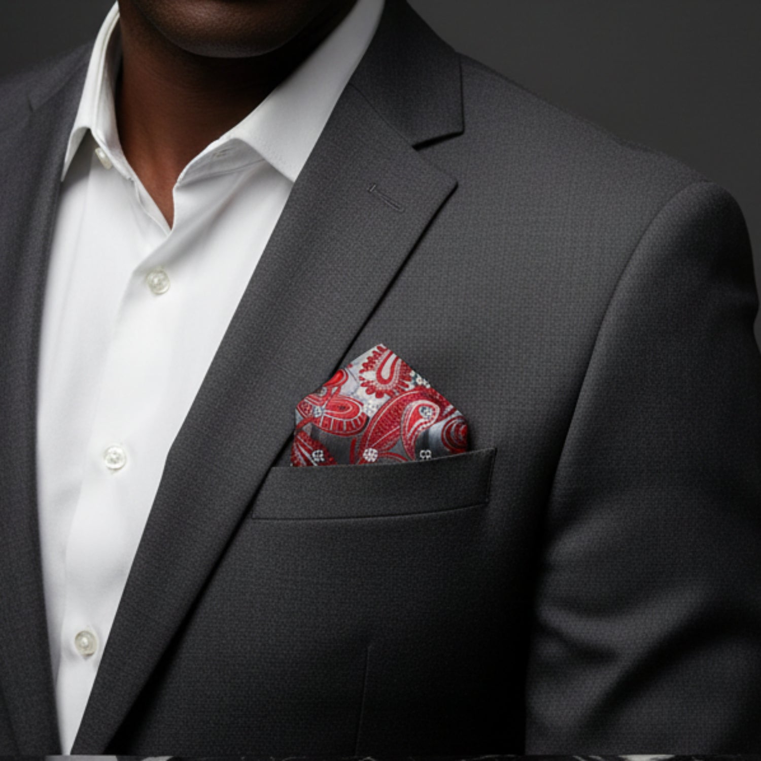 Man wearing a gray suit with a red paisley pocket square against a dark background