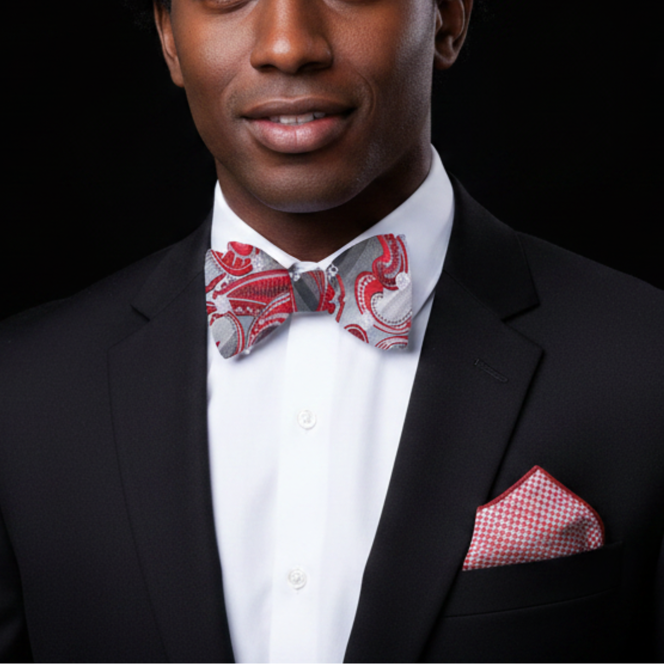 Man wearing a black suit with a red and white patterned bow tie and pocket square on a black background