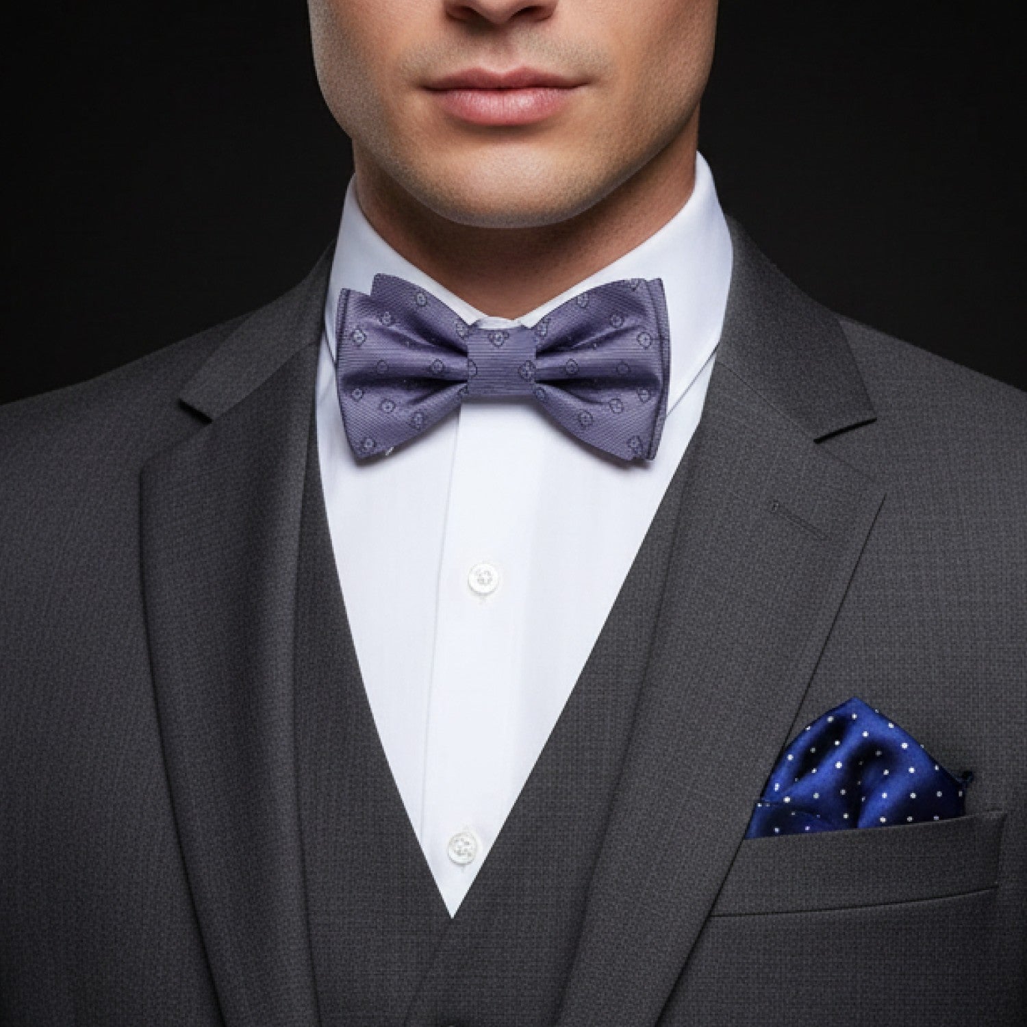 Man wearing a gray suit with a grey bow tie and matching pocket square against a black background