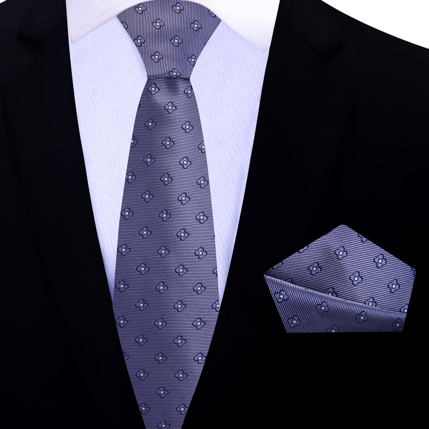 Grey floral patterned thin tie and pocket square set on a black suit jacket.