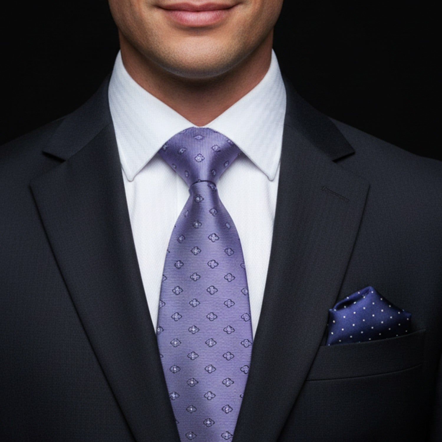 Man wearing a dark suit with a white shirt, grey tie, and accenting pocket square.