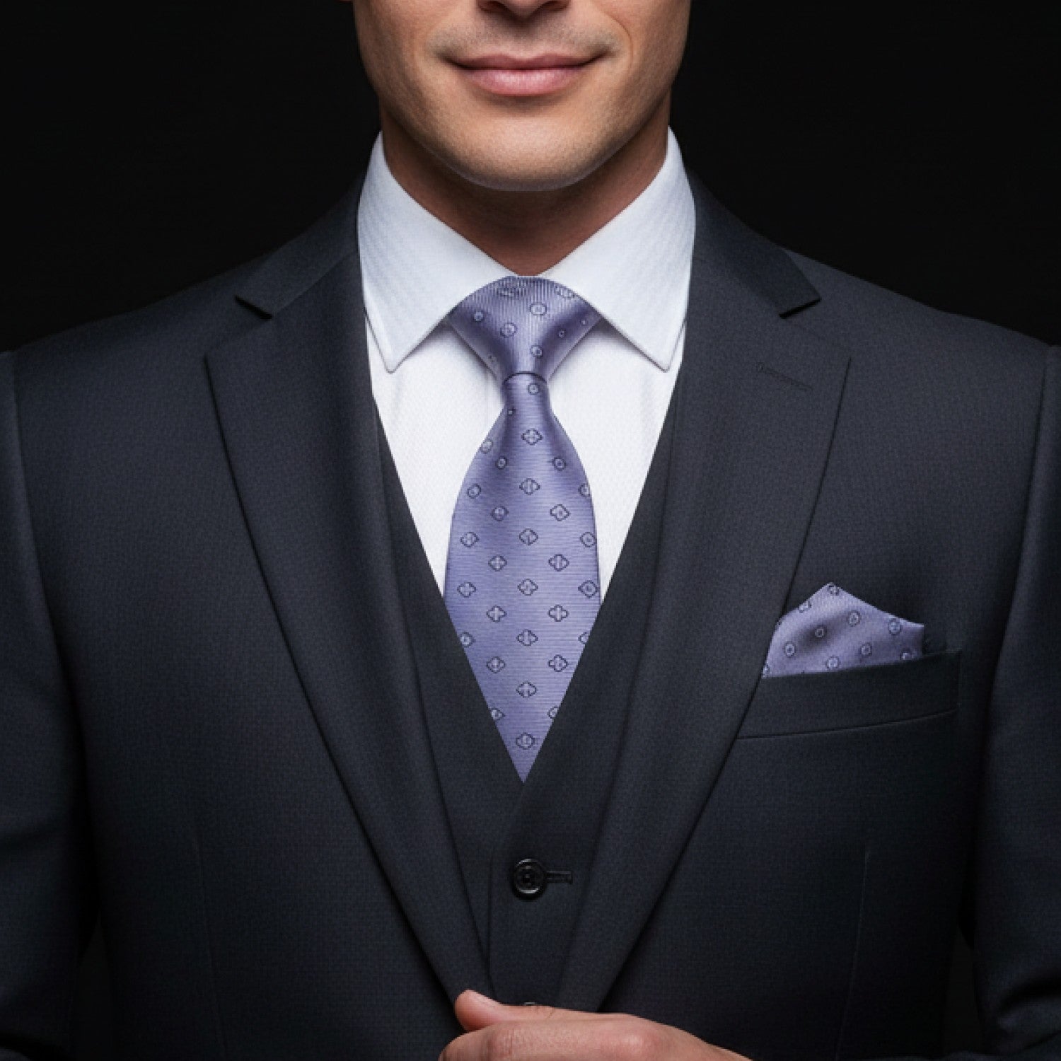 Man wearing a dark suit with a light grey floral tie and pocket square on a black background